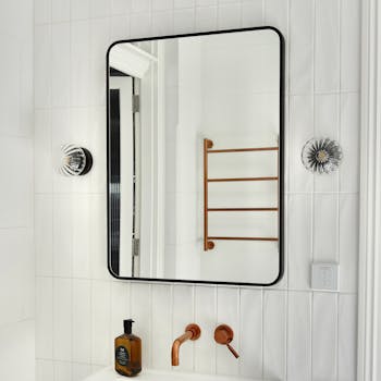 A stylish bathroom interior featuring a mirror, copper faucet, and wall-mounted lights.